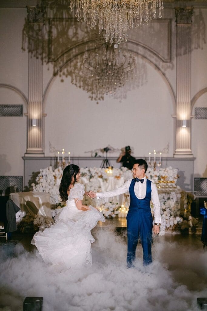 Bride and groom dancing on a fog-filled dance floor beneath a crystal chandelier at their wedding reception