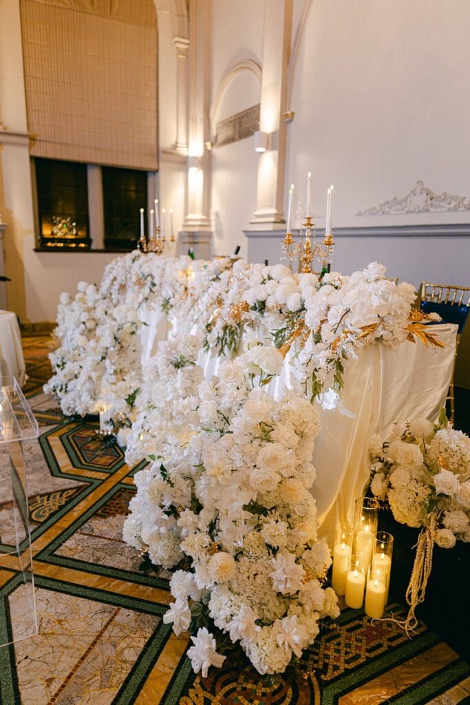 Cascading white floral table runner with gold candelabra styled along a wedding reception table