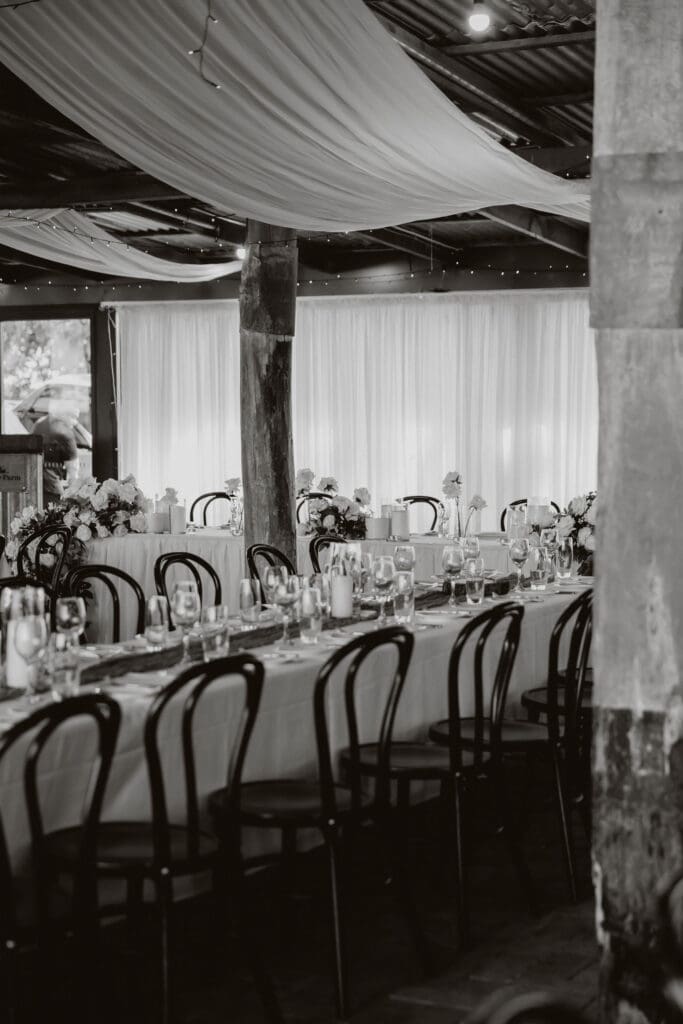 Long reception table styled with white florals, candles and black bentwood chairs at a rustic barn wedding venue
