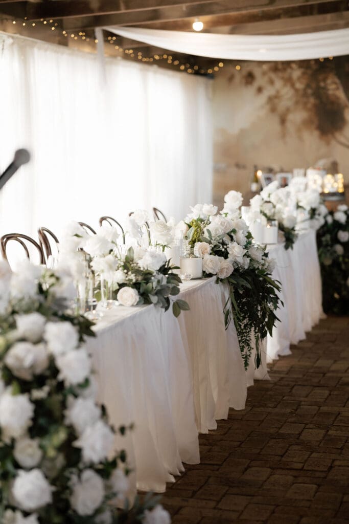 Faux flower and greenery garland styled along a wedding feasting table with pillar candles and fairy lights